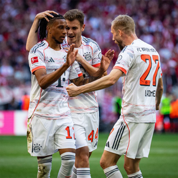 Three football players from Bayern Munich celebrate together after a successful play. They are smiling and showing excitement, with one player receiving a congratulatory gesture. The scene captures a moment of camaraderie and team spirit during a match.